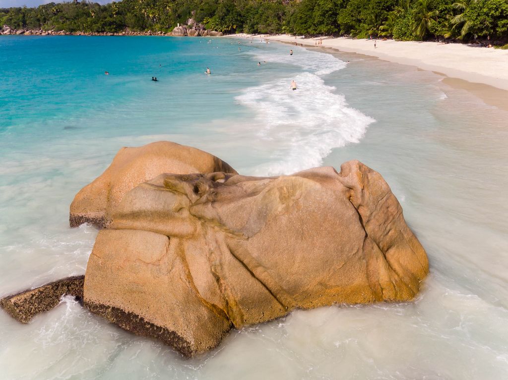 Close-up of a granite rock next to Anse Lazio Beach with swimming tourists in the back in Praslin, Seychelles