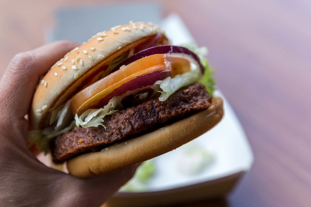 Close-up of a hand holding the new Big Vegan TS McDonalds Burger in Germany, with soy patty, tomato slices, mustard sauce and Lollo Bionda salad