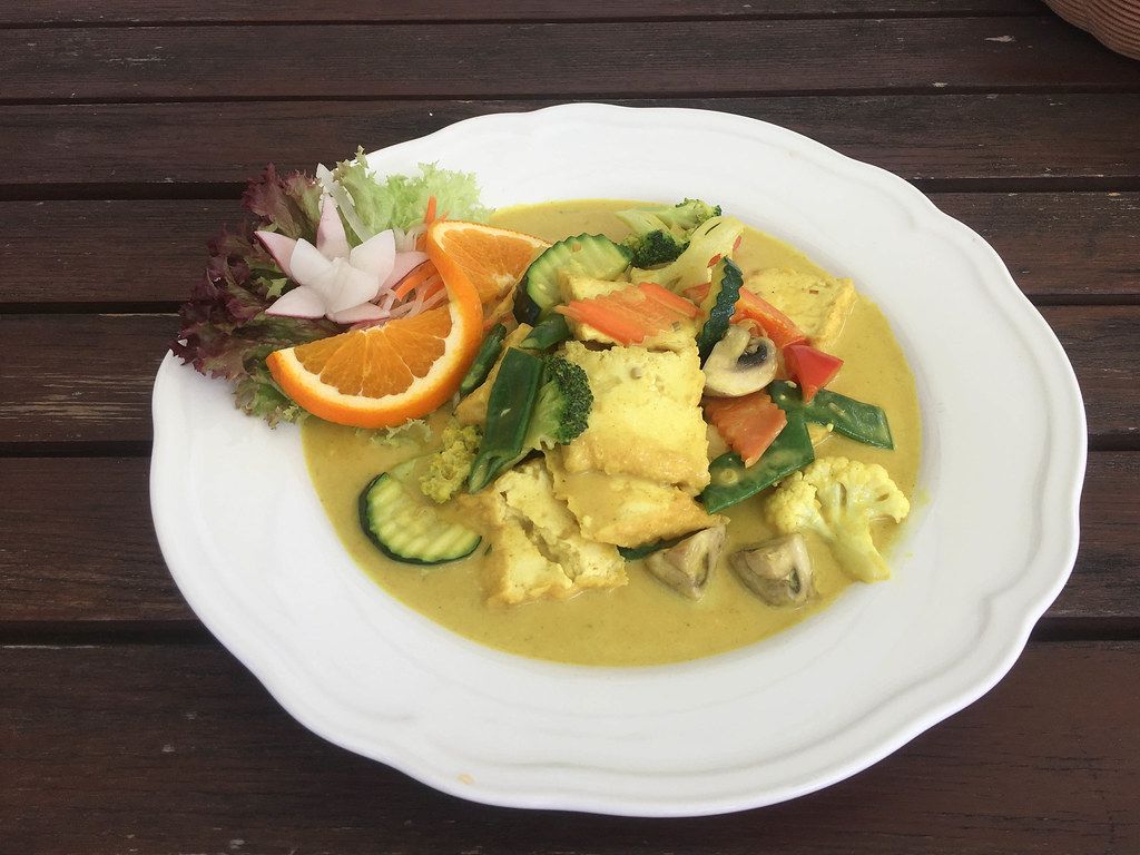 Close-up of a lunch for vegan diet and balanced nutrition, with healthy vegetables, mushrooms and orange in a curry turmeric sauce, on a white plate