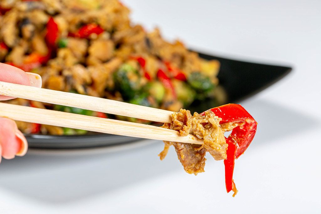 Close-up of chicken with vegetables in spicy sauce and chopsticks. The concept of Chinese food