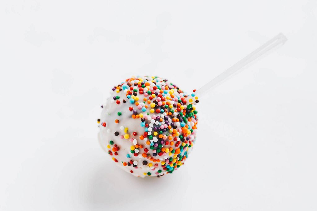Close up of lollipop with colorful sprinckles on white background