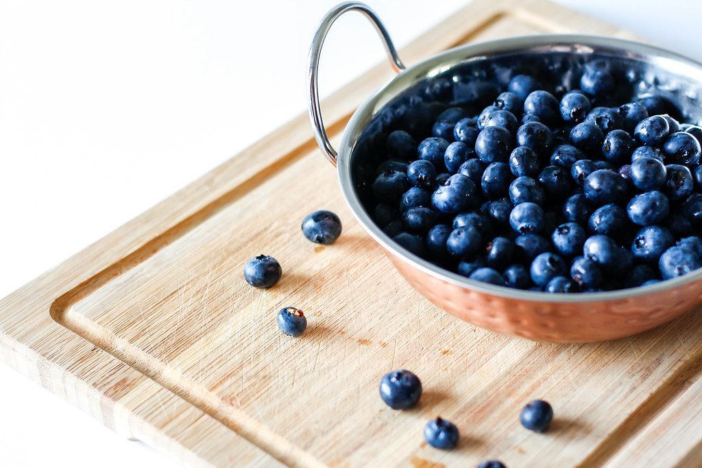 Close Up Photo of Fresh Washed Blueberries in Bowl on Wooden Cutting Board on White Background