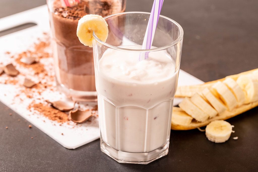Close Up Photo of Glass with Banana Milk Shake with Sliced Banana next to it