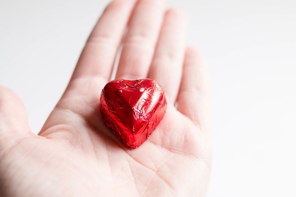 Close Up Photo of Heart shaped Chocolate wrapped in Red Foil laying on a Hand