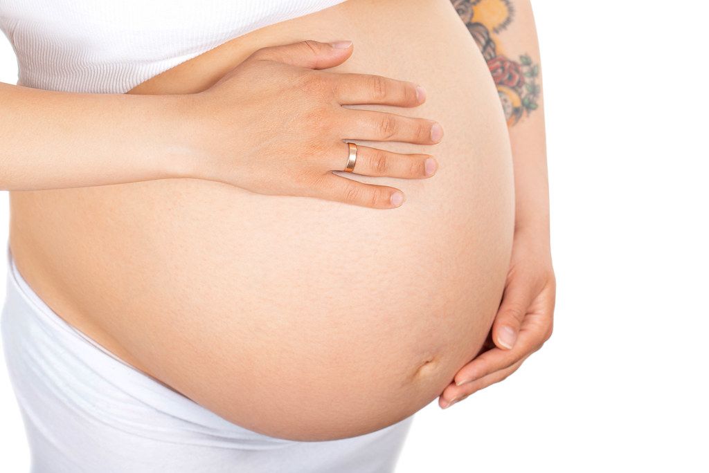 Close-up pregnant woman's belly on white background. Pregnancy, parenthood, preparation and expectation concept