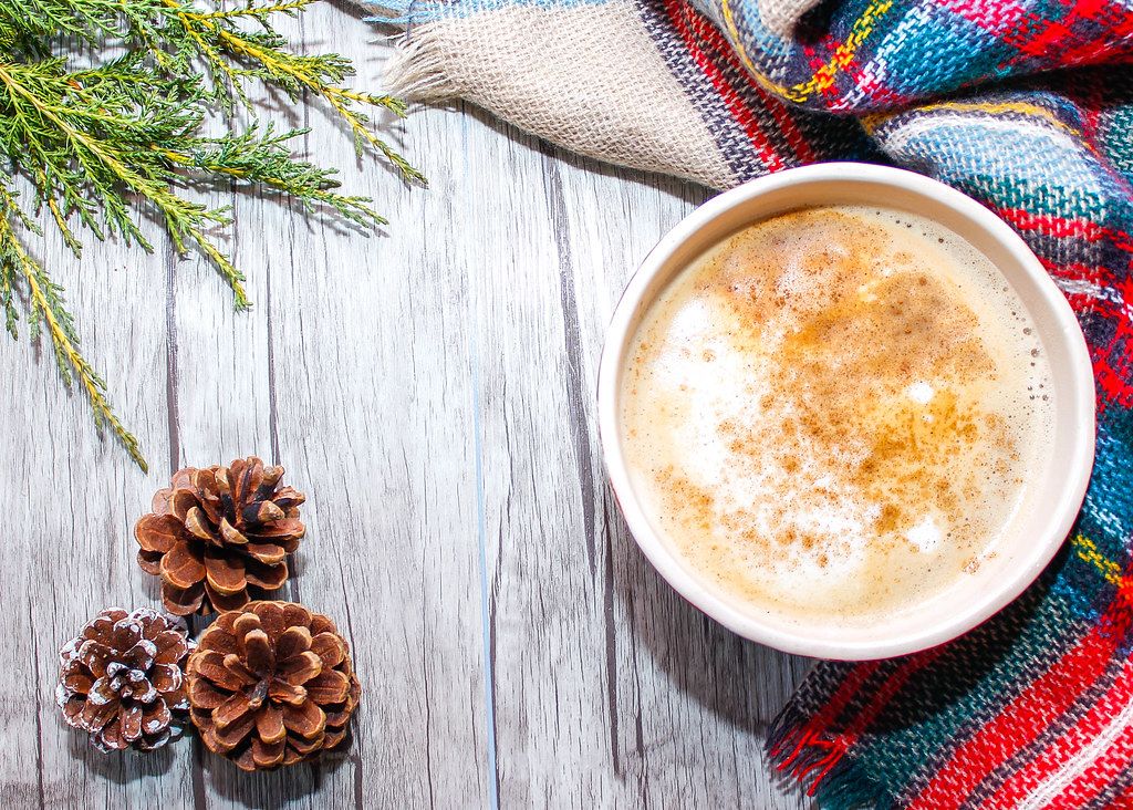 Close Up Top View Photo of Large Coffee Cup next to Scarf and Pinecones on Wooden Background