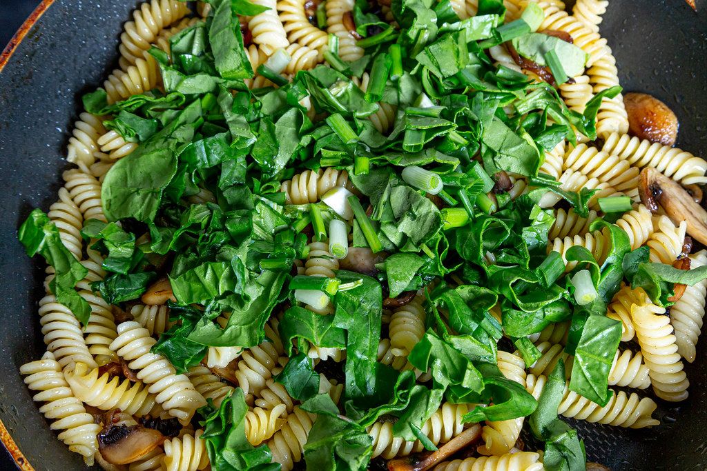 Closeup of pasta with spinach and mushrooms in a frying pan
