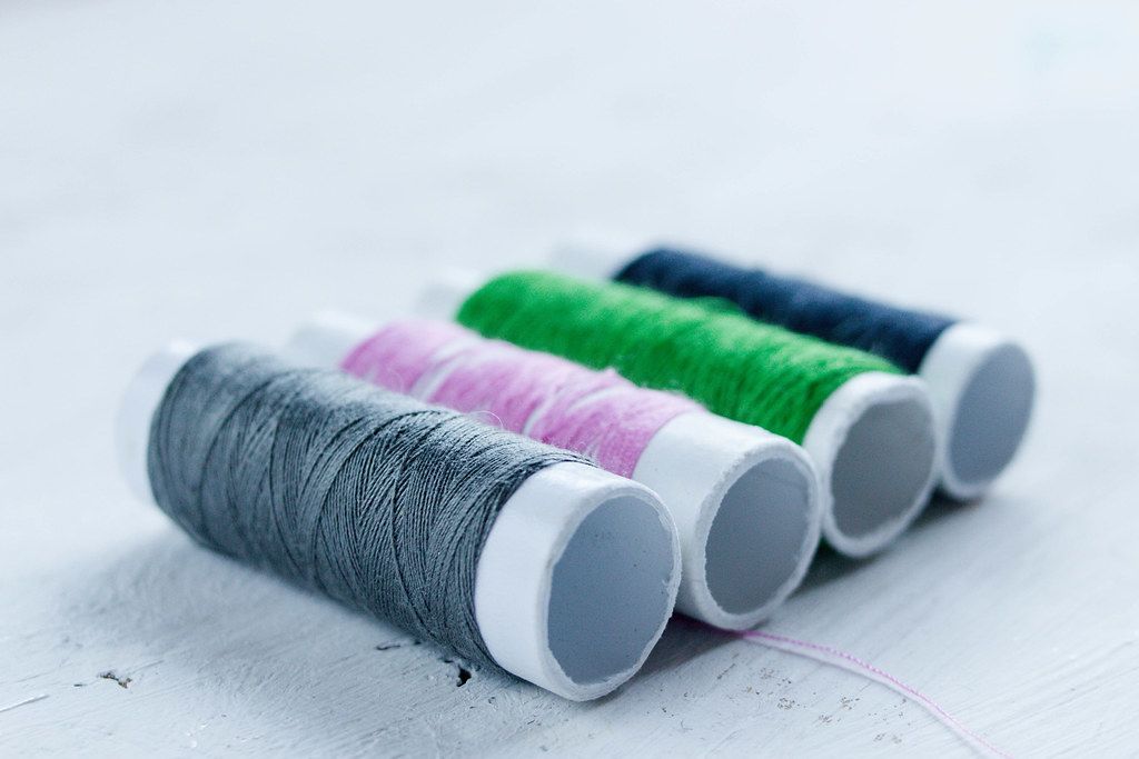 Colorful sewing thread grey, pink, green and navy on a white wooden surface