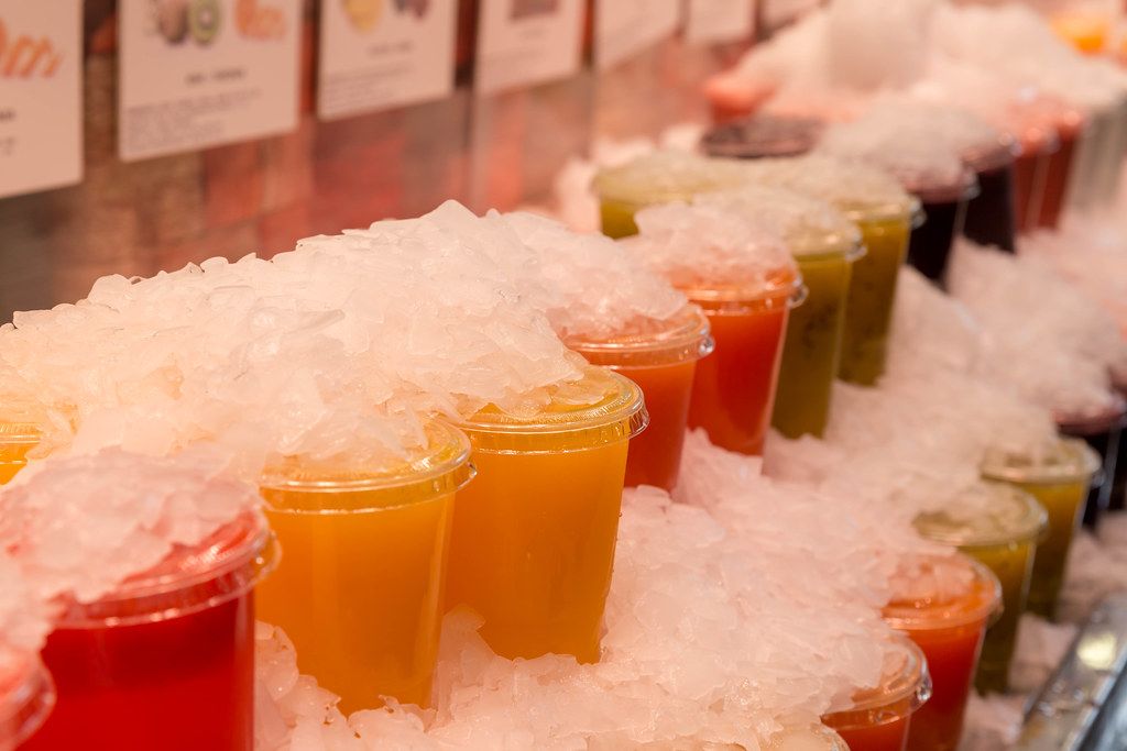 Colorful smoothie juice drinks in plastic cups under crushed ice at the Spanish Boqueria Market 