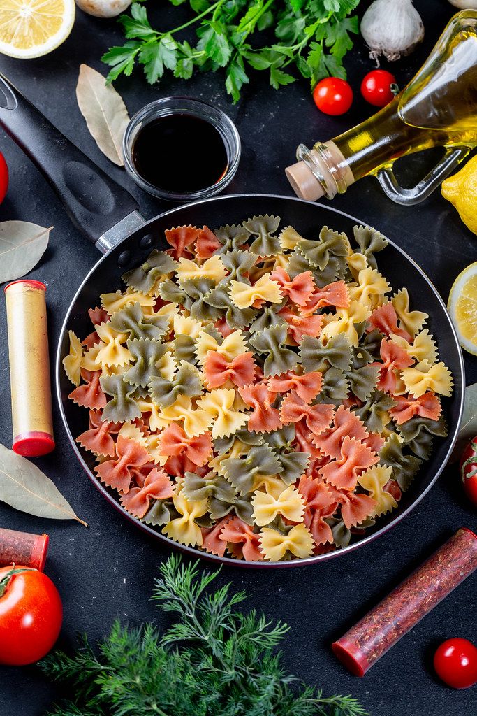 Cooking on a black background. Pasta with spices, vegetables and herbs. Top view