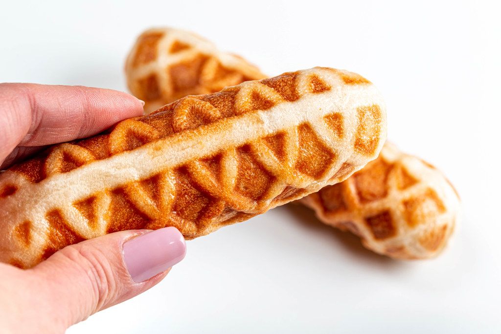 Corn dog in a waffle close-up in a female hand