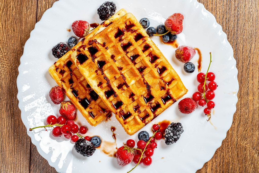 Crispy Belgian waffles with chocolate topping and ripe berries on a white plate. Top view (Flip 2019)