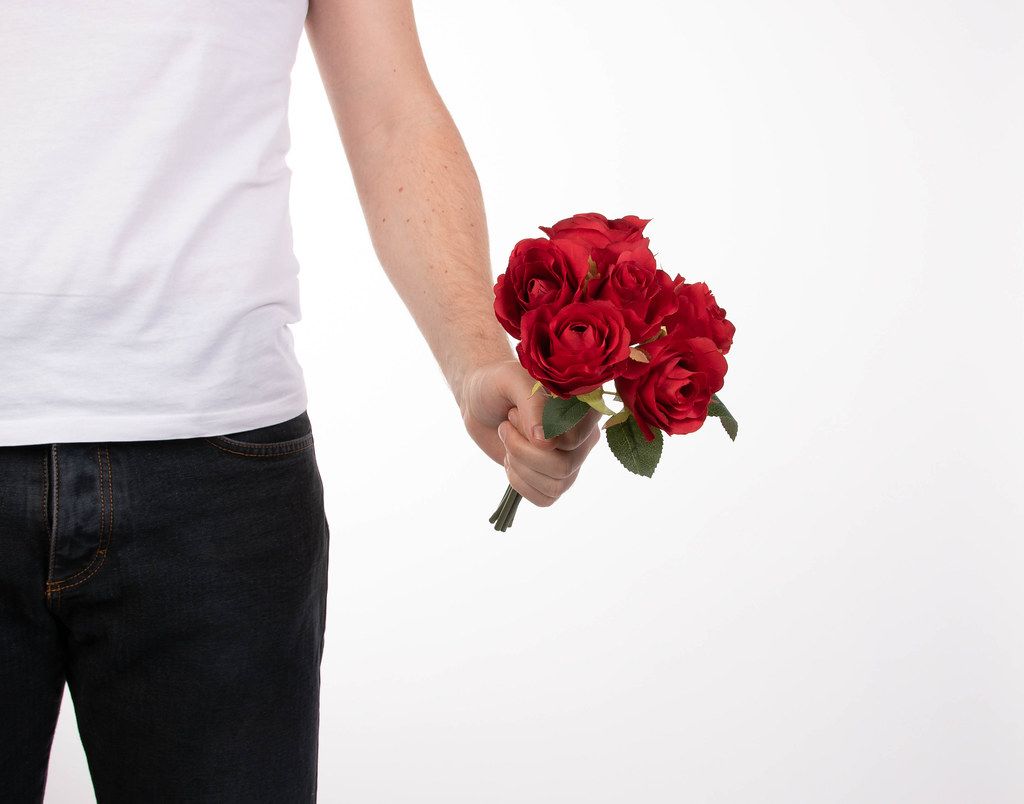 Cropped shot of a young man's arm holding out a bunch of red roses