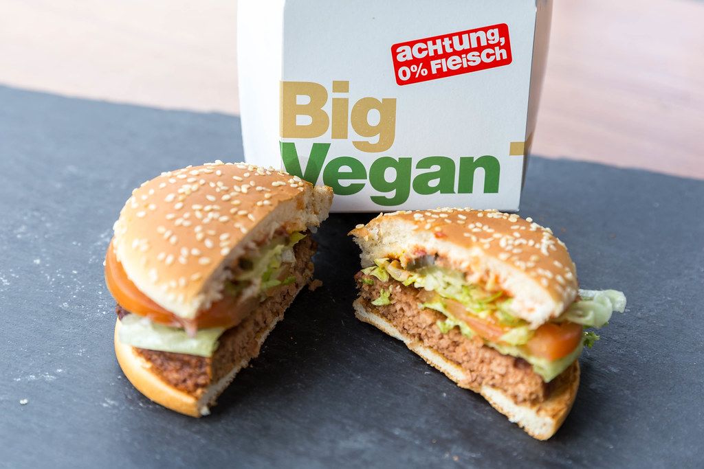 Cut in half Big Vegan TS by McDonalds with a patty based on soy and wheat protein, with salad, vegetables & sesame bread, in front of a burger box