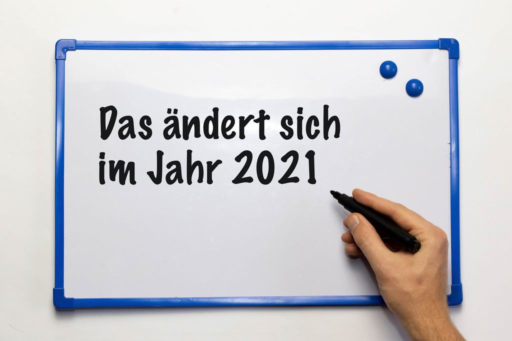 'Das ändert sich im Jahr 2021'-Schriftzug auf Weißwandtafel mit schwarzen Whiteboard-Marker in männlicher Hand - Nahaufnahme zentral