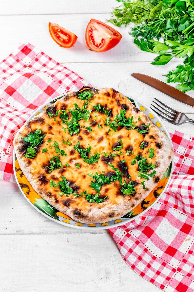 Delicious baked khachapuri with kitchen appliances, herbs and tomatoes