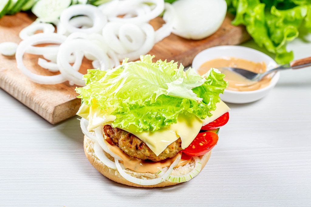 Delicious fresh homemade burger with lettuce, cheese, onion and tomato on a white wooden background