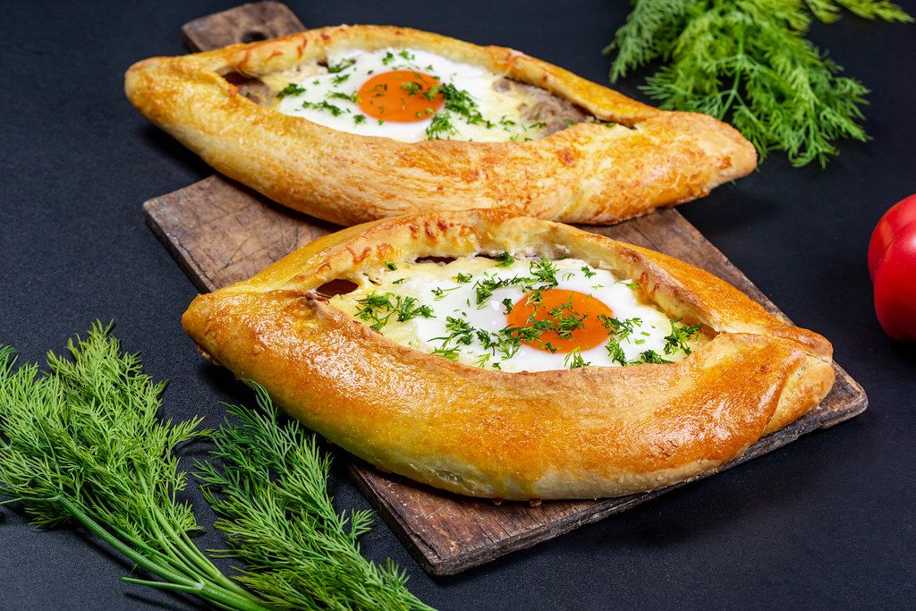 Delicious homemade Adjarian khachapuri on a dark background with green dill
