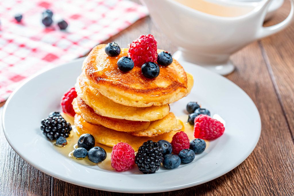 Delicious homemade golden pancakes with fresh raspberries, blueberries and mulberry