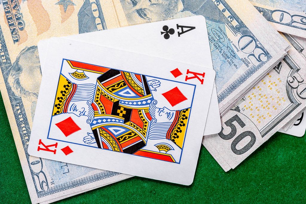 Die zwei Spielkarten Ass und König, liegen auf Dollarscheinen auf einem grünen Pokertisch