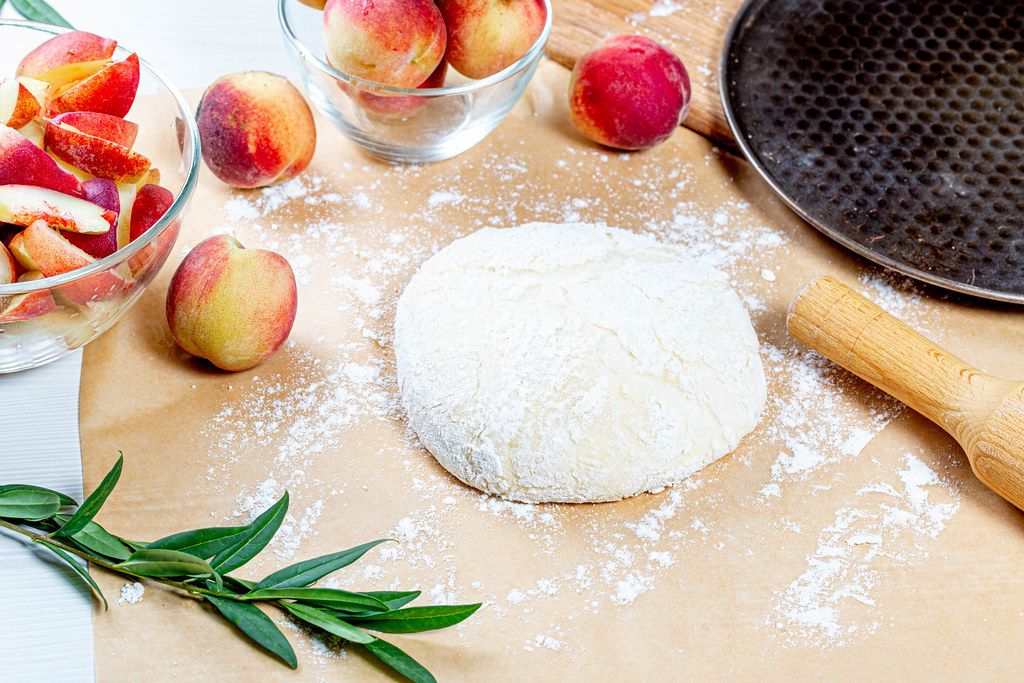 Dough-flour-and-fresh-peaches-with-rolling-pin-and-baking-sheet-on-the-table.jpg