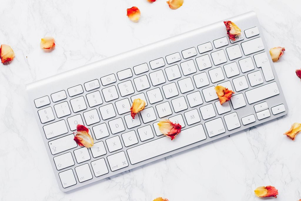 Draufsicht einer Tastatur mit Blütenblättern einer Rose auf Marmor