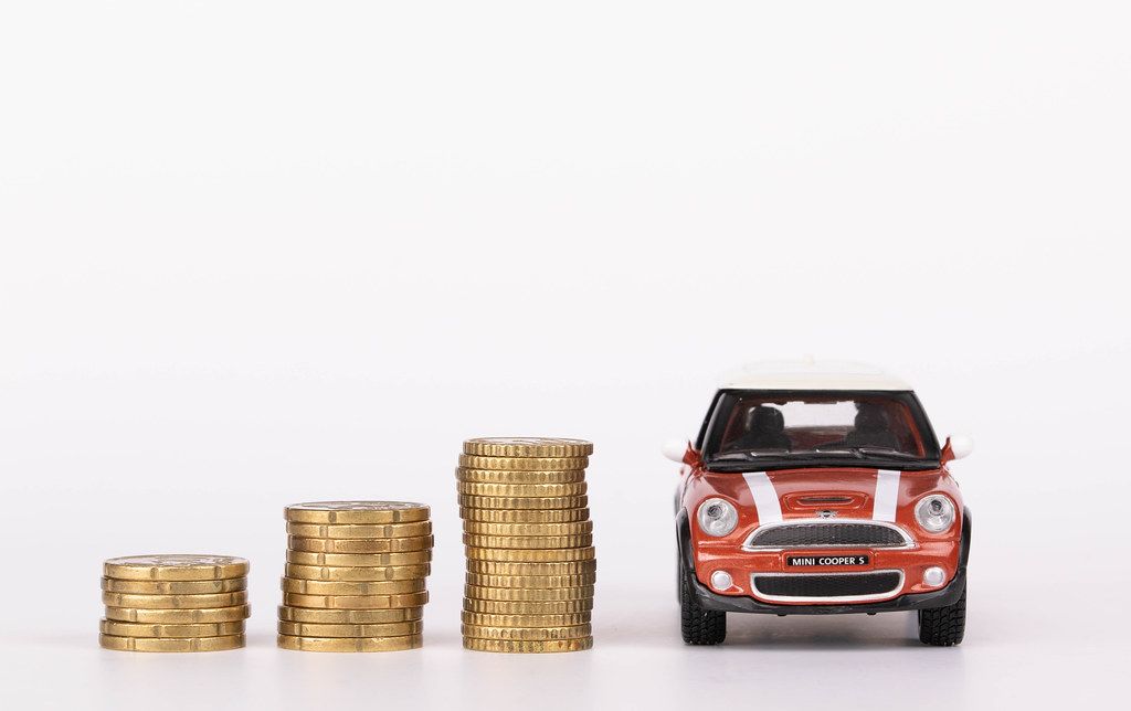 Drei Stapel 20-Cent und 50-Cent Münzen und Mini Cooper S Spielzeugauto vor weißem Hintergrund
