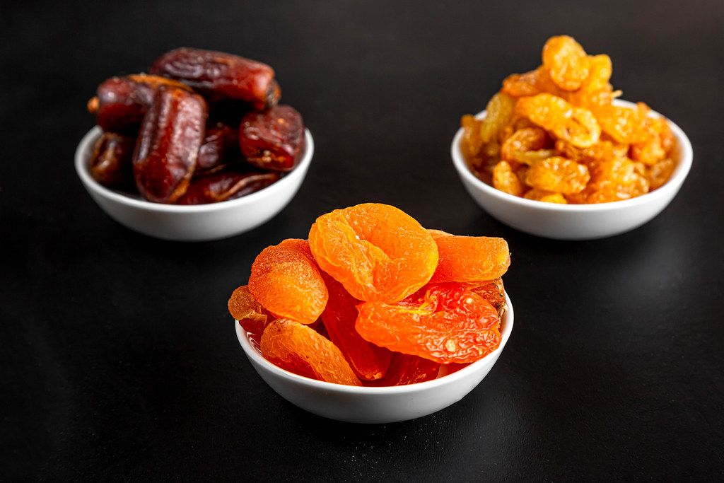 Dried apricots, raisins and dates in white masks on a black background