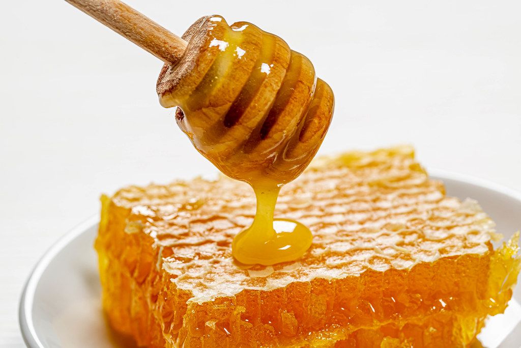Dripping honey on honeycomb on white plate
