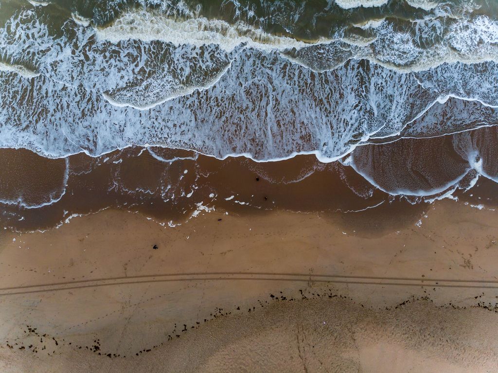 Drohnenaufnahme Sandstrand mit hereinrollenden Wellen