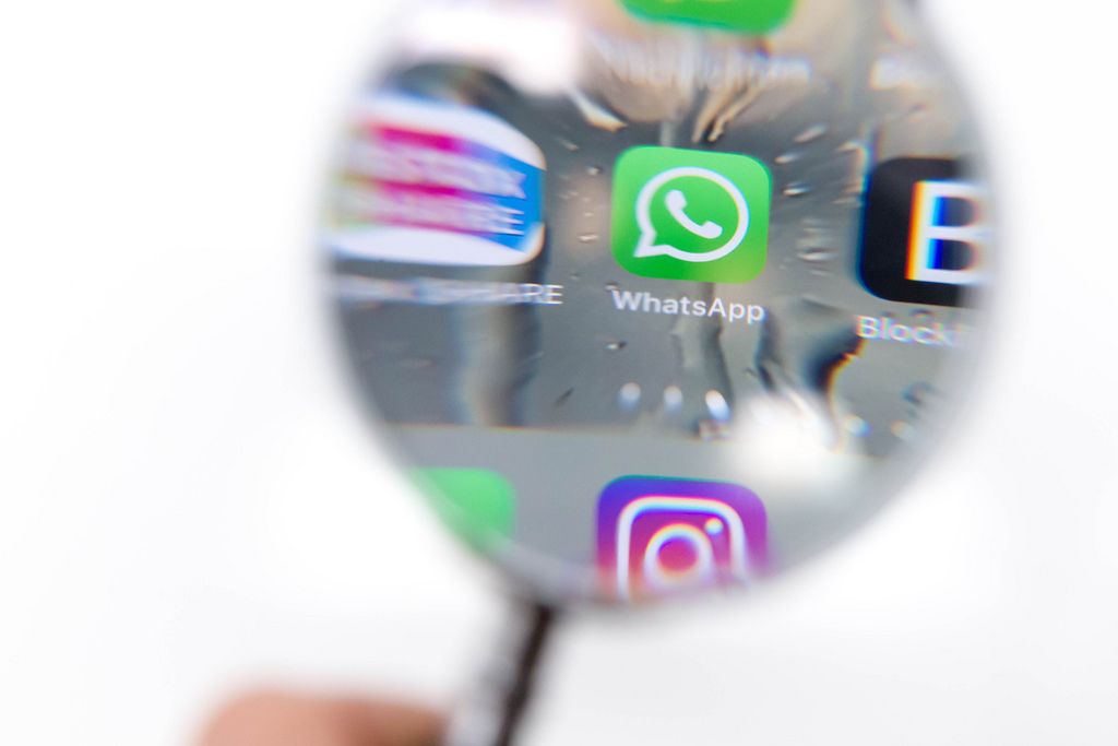 Durch Lupe fotografiertes WhatsApp Icon auf Telefon vor weißem Hintergrund