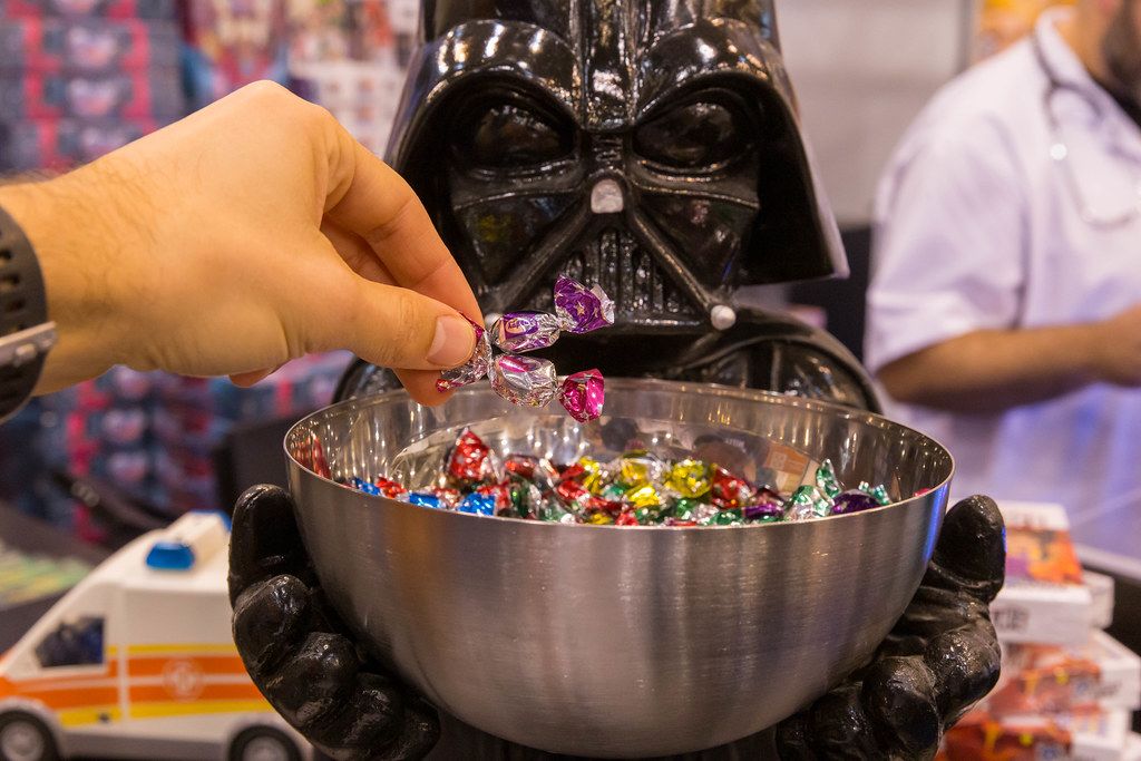 Ein Mann greift in eine Süßigkeitenschale nach Bonbons die von einer Darth Vader Figur gehalten wird