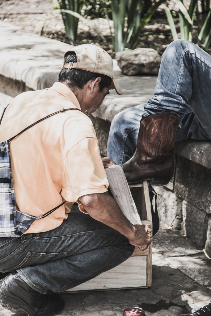 Ein Schuhputzer poliert die Cowboystiefel eines Mannes im Park in Honduras