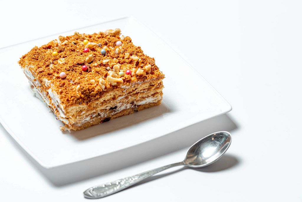 Ein Stück selbstgemachter Honigkuchen auf einem weißem Teller mit Löffel auf weißem Hintergrund