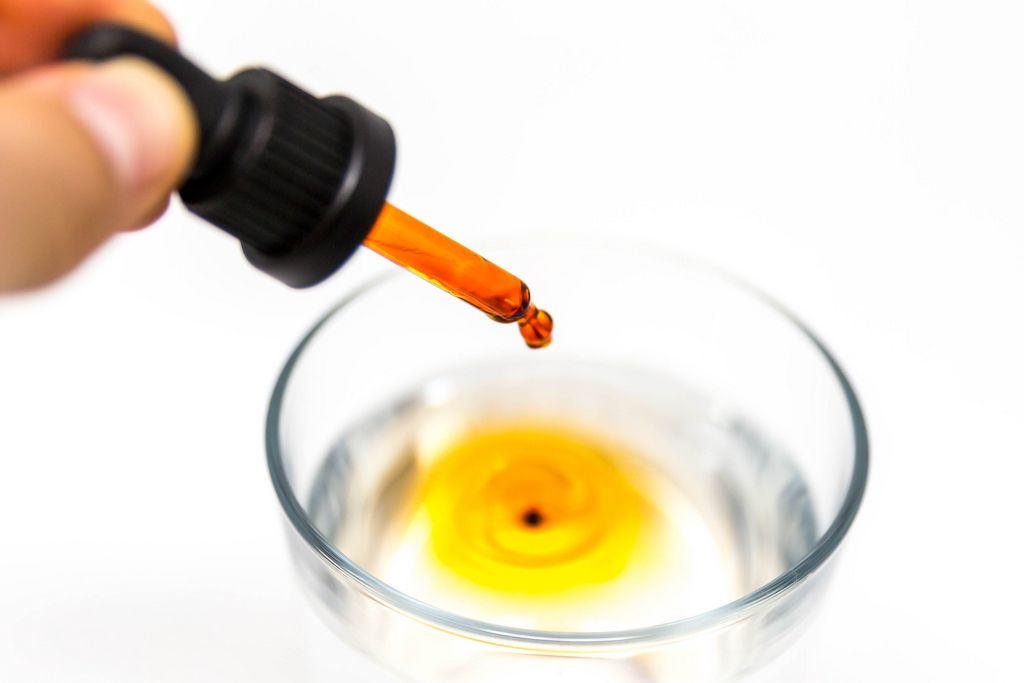 Ein Tropfen Braineffect Recover Cannabidiol (CBD) Öl färbt das Wasser im Glas orange