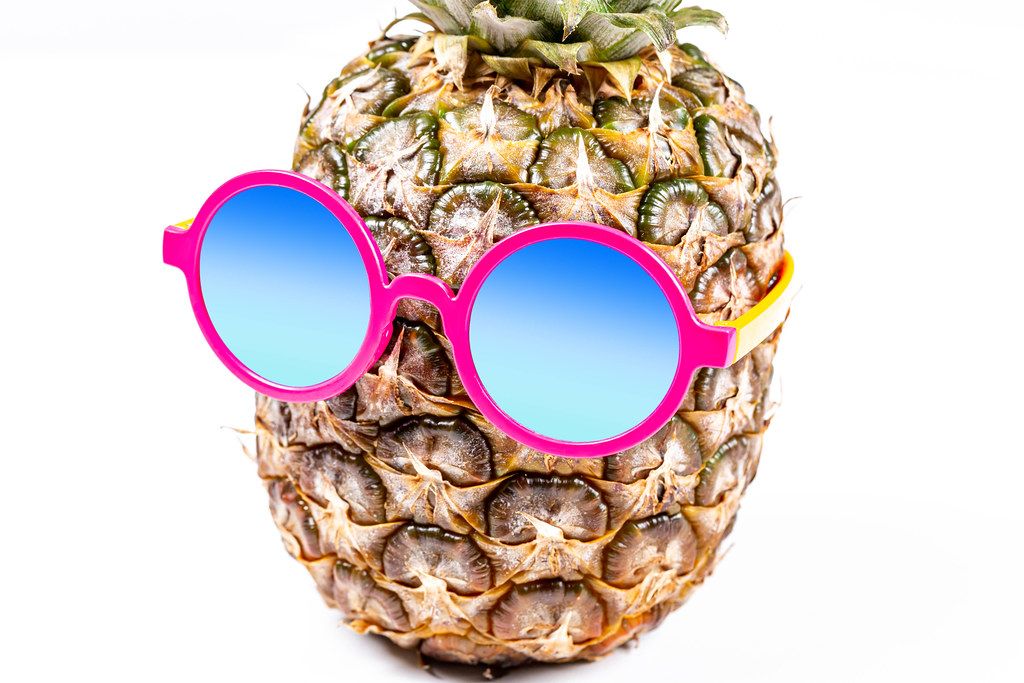 Eine Ananas trägt eine rosa Sonnenbrille vor weißem Hintergrund