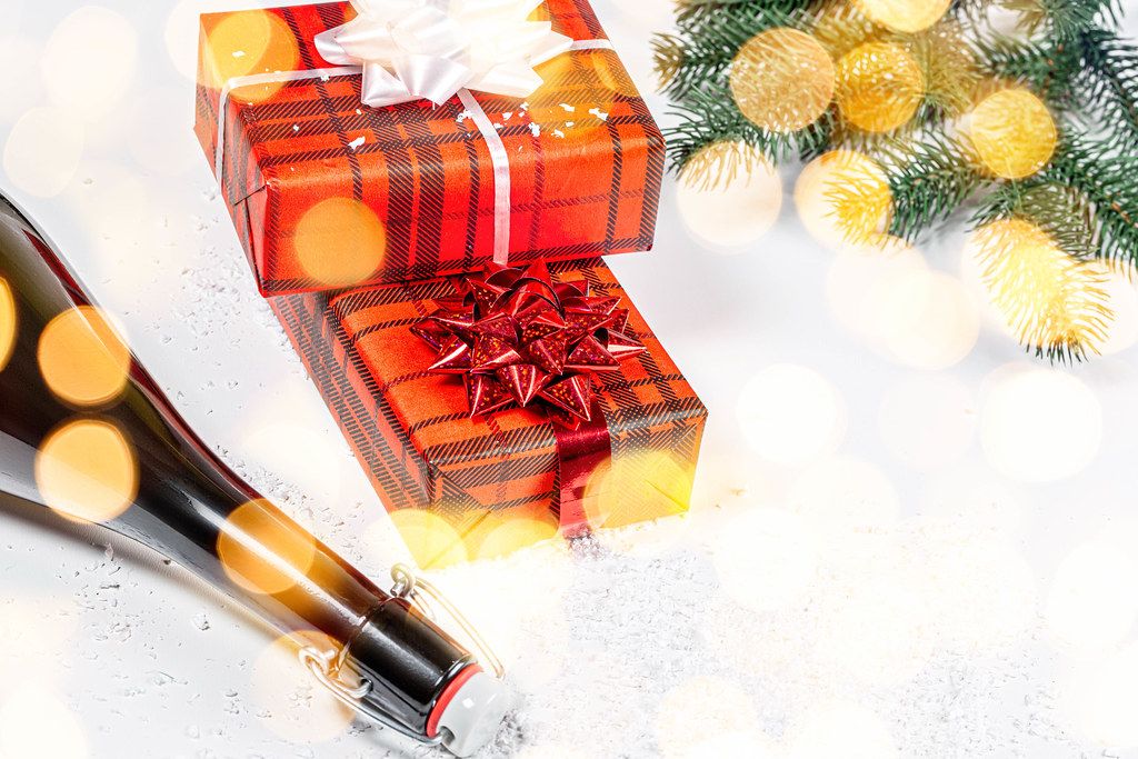 Eine Flasche Champagner und zwei Geschenkboxen - Das Konzept von Weihnachten vor einem Schneehintergrund mit bokeh und Tannenzweigen