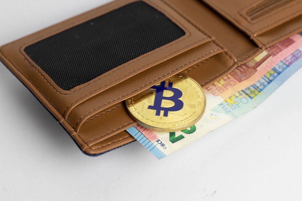 Eine goldene Bitcoinmünze in einer Geldbörse mit Euroscheinen