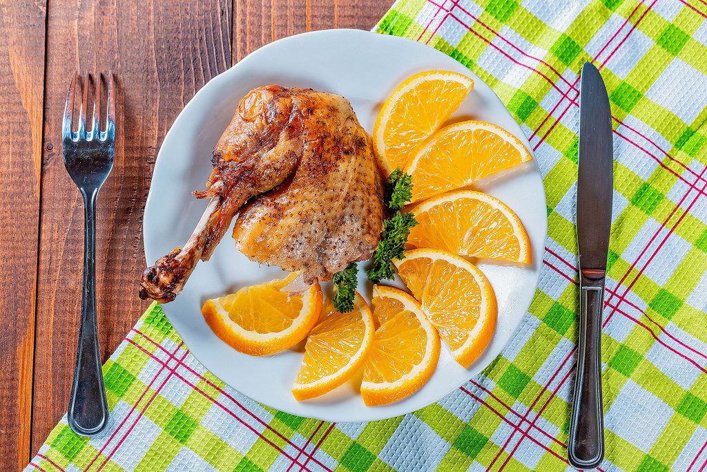 Eine Hähnchenkeule mit Orangenscheiben und Petersilie auf einem Teller mit Messer und Gabel auf einem Tisch