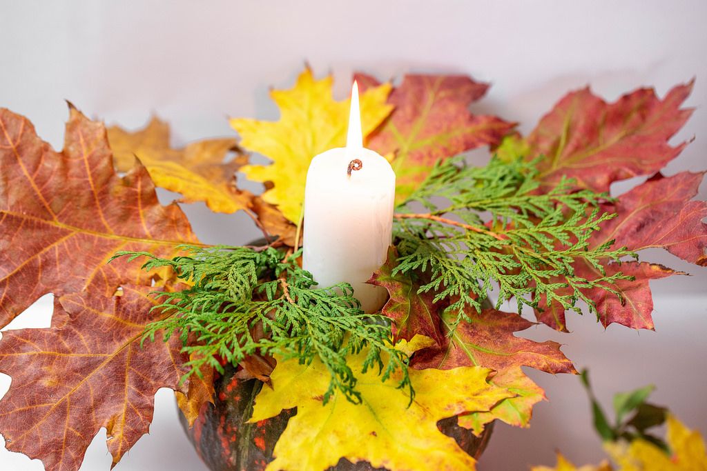 Eine Kerze leuchtet auf einem Kürbis mit Tannenzweigen und bunten Blättern