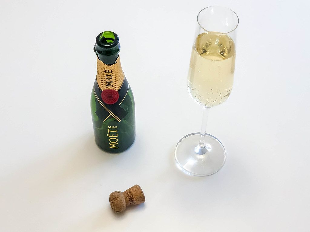 Eine leere Flasche Mini Moët mit seinem Korken und ein volles Champagnerglas auf weißem Hintergrund