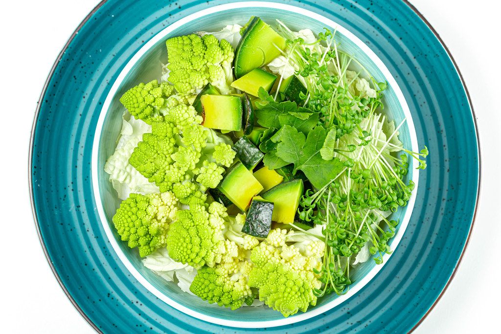 Eine Schüssel mit frischem Salat, Romanesco Kohl, Avocado, Petersilie und Wasserkresse auf einem Teller von oben fotografiert