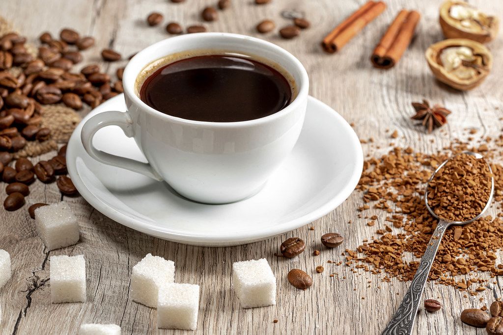 Eine Tasse heißer Kaffee mit ganzen und gemahlenen Kaffeebohnen, Zucker und Gewürzen auf einem Holzhintergrund