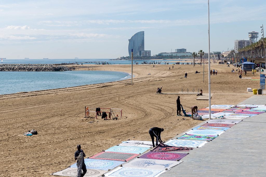 Einheimische Straßenhändler verkaufen Teppiche am Platja del Somorrostro Sandstrand vor dem Mittelmeer in Barcelona, Spanien