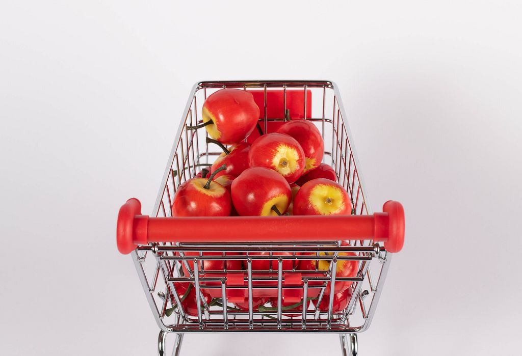 Einkaufswagen gefüllt mit süßen roten Äpfeln vor weißem Hintergrund