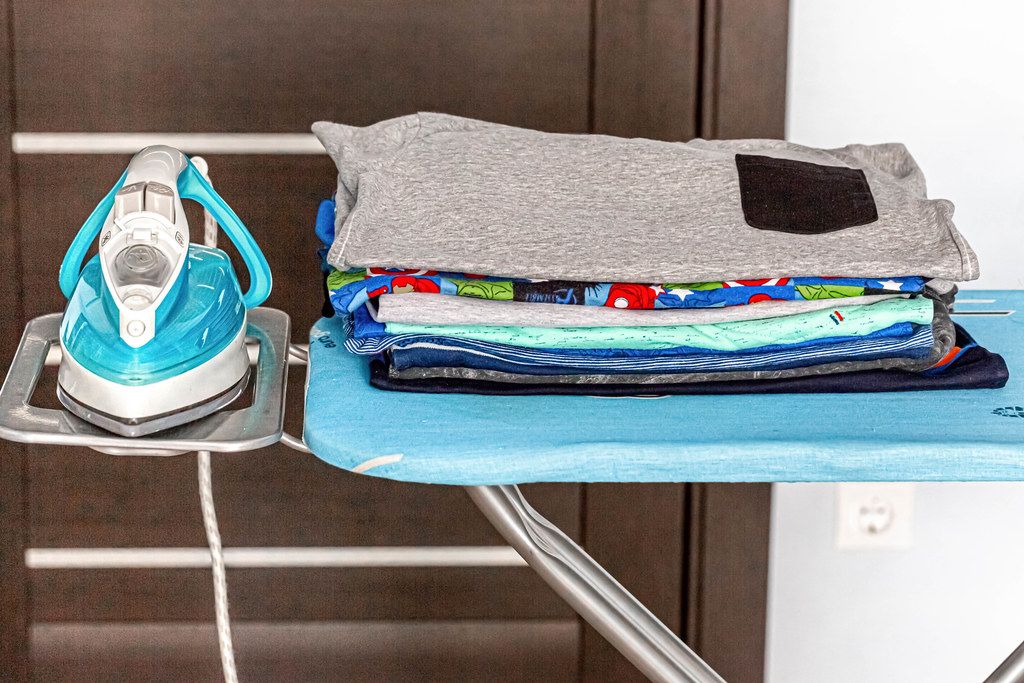 Electric iron with a stack of ironed clothes on blue ironing board