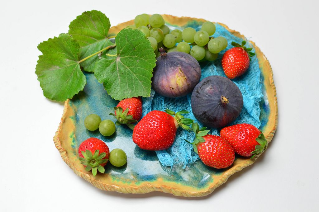 Feigen mit Erdbeerenund Weintrauben geschückt mit Weinblättern auf blauem Tonteller