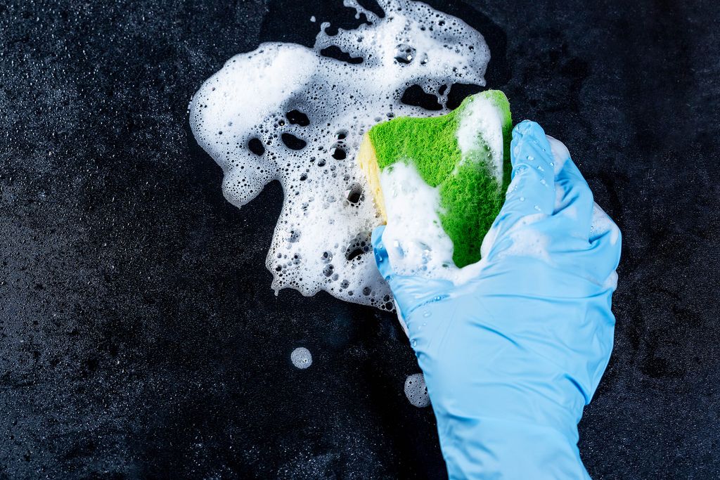 Female hand in gloves with sponge and soap foam on dark background