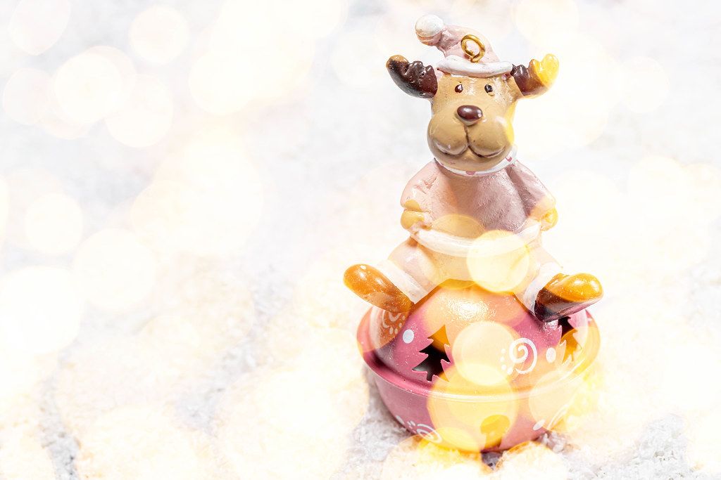 Festive winter background toy-deer on white snow with Golden bokeh background