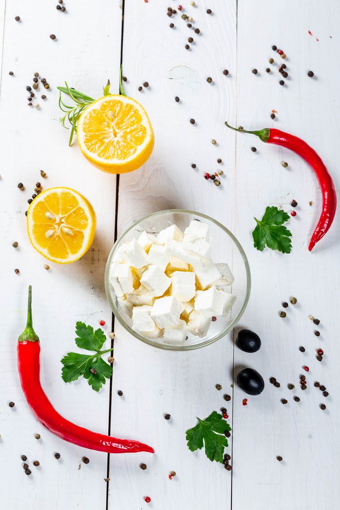 Feta cheese, chili, olives, parsley and peppers on white wooden background